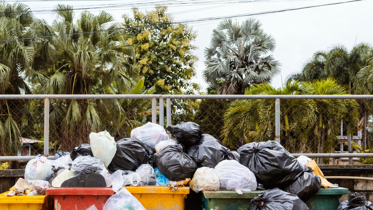 Overflowing trash bins filled with plastic bags and garbage in an outdoor area